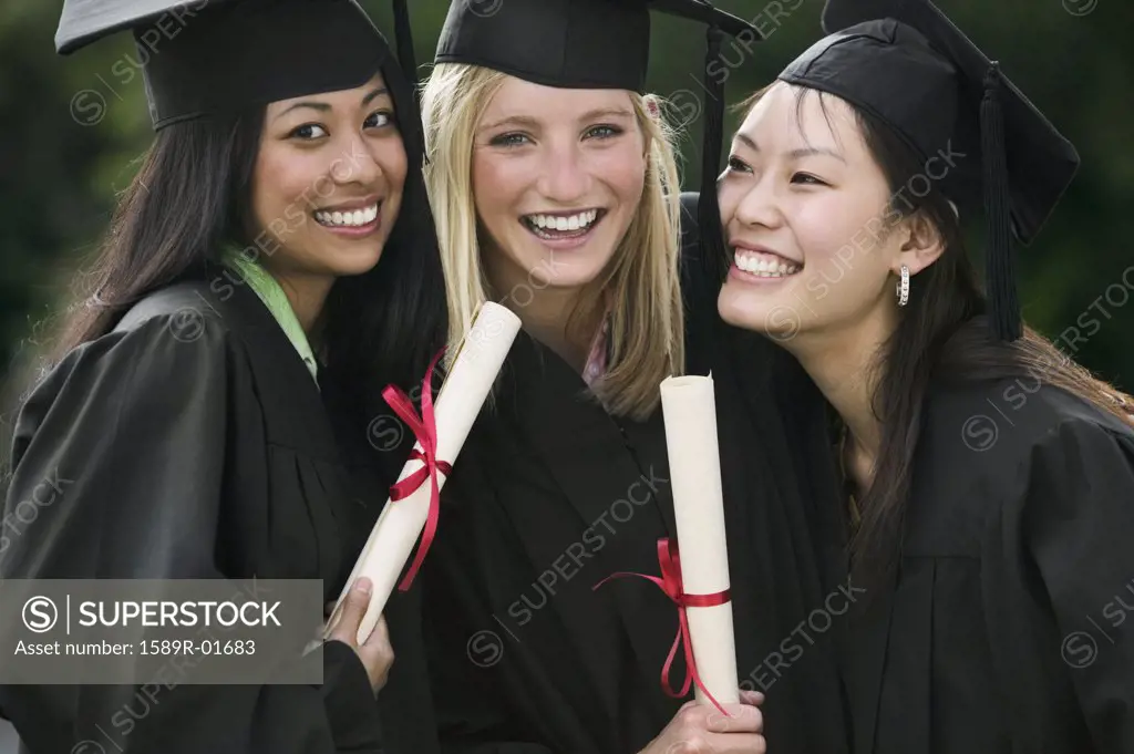 Three young female graduates standing together holding diplomas smiling