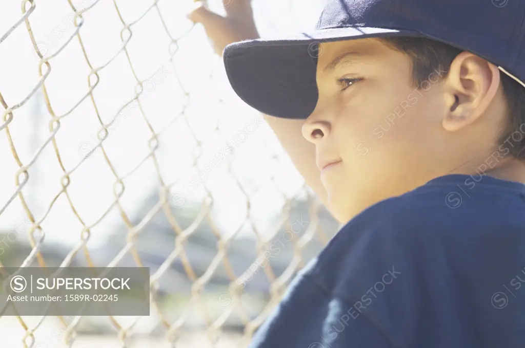 Young boy standing holding a chain link fence