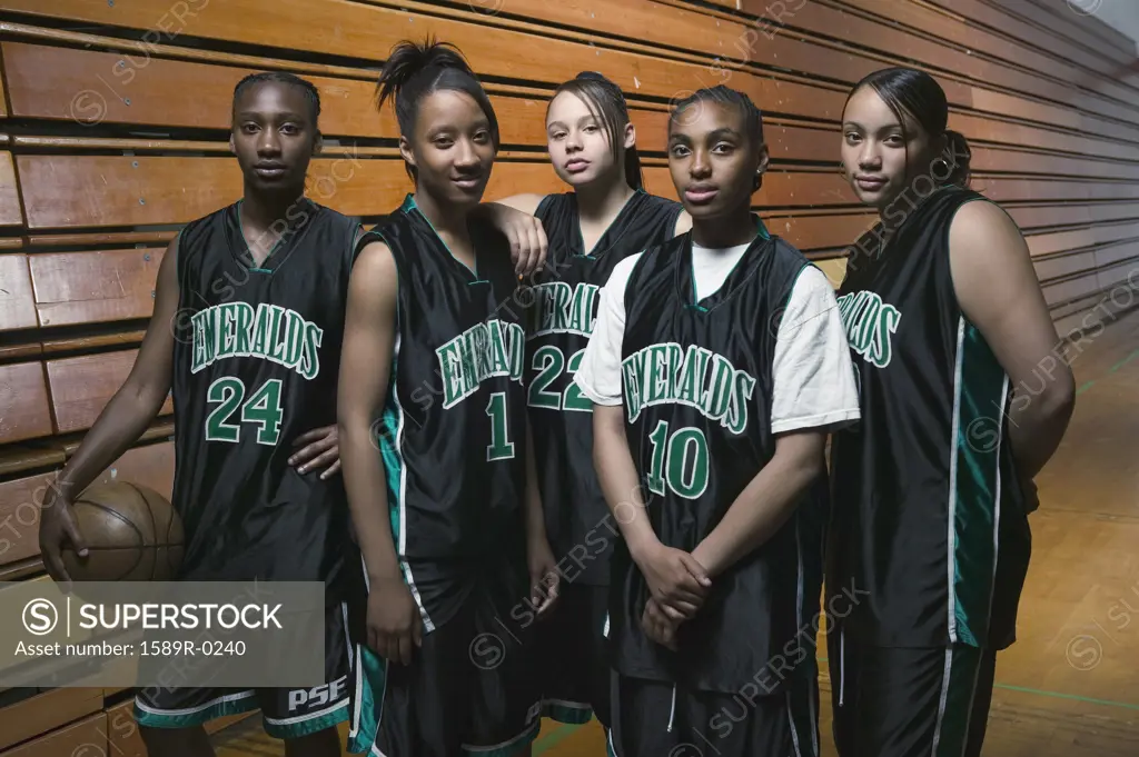 Team of female teenage basketball players posing on a basketball court