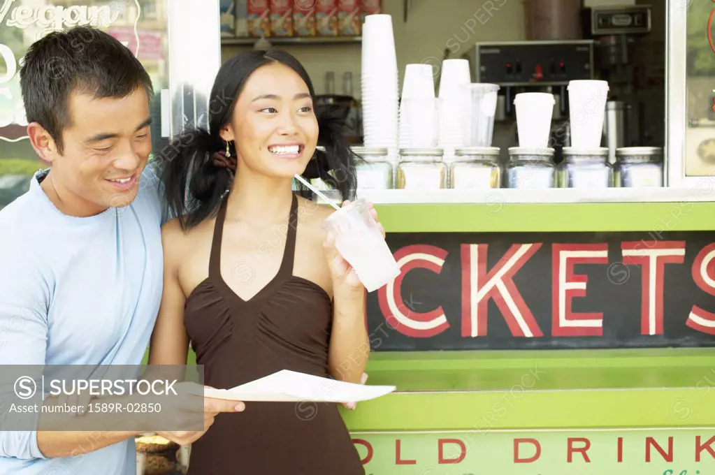 Mid adult man and a young woman standing together at a food and drinks stall reading a menu