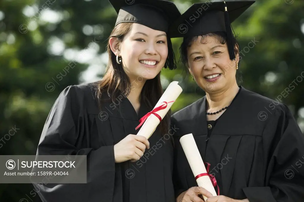 Two female graduates standing together holding diplomas smiling