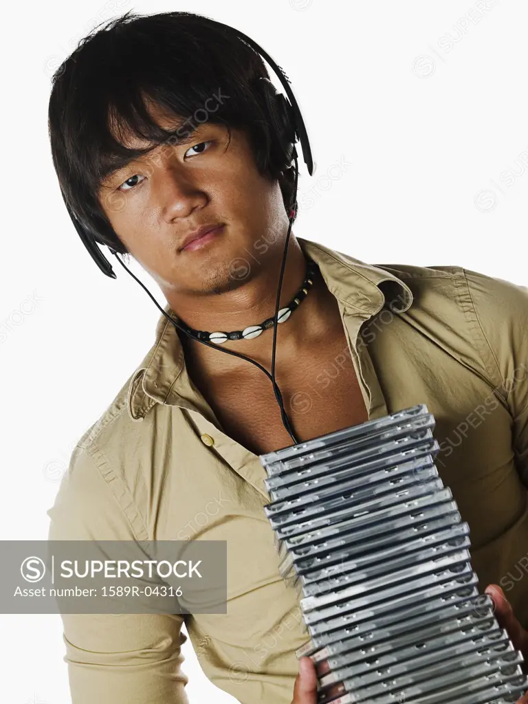 Portrait of a young man wearing headphone holding a stack of compact discs