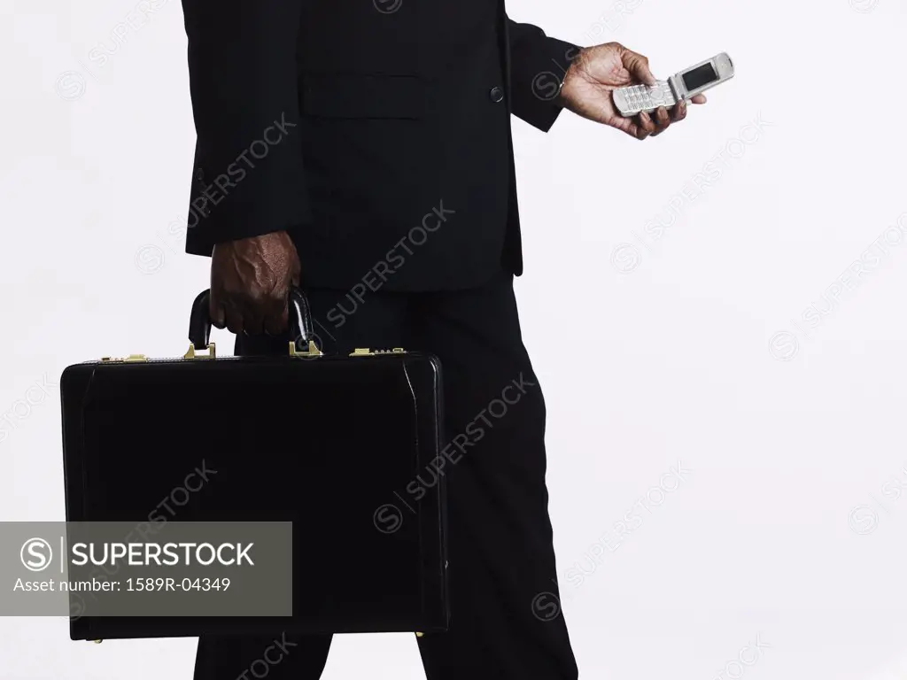 Man walking holding a briefcase and operating a mobile phone