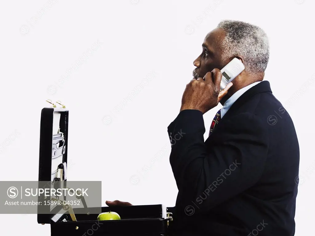 Side profile of an elderly man talking on a mobile phone with an open briefcase in front of him
