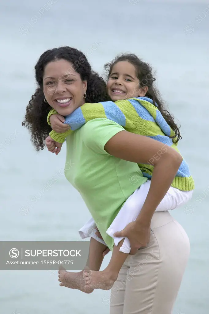 Young girl piggyback riding on a young woman at the beach