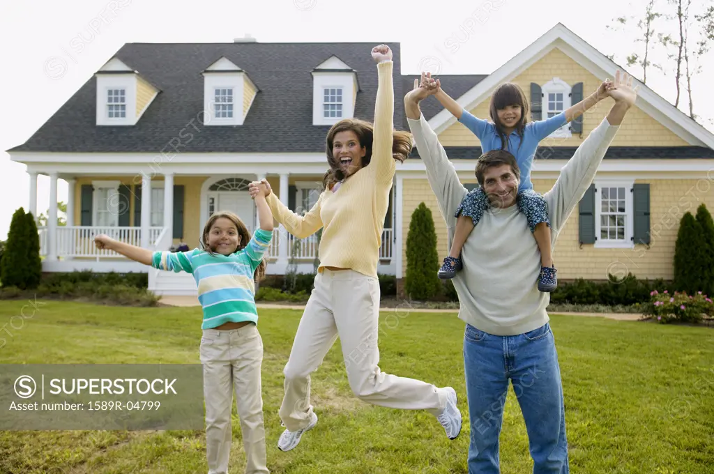 Young couple playing with their children on a lawn in front of a house
