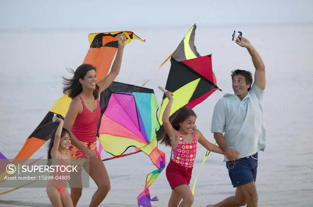 Young couple running on the beach with their children holding kites