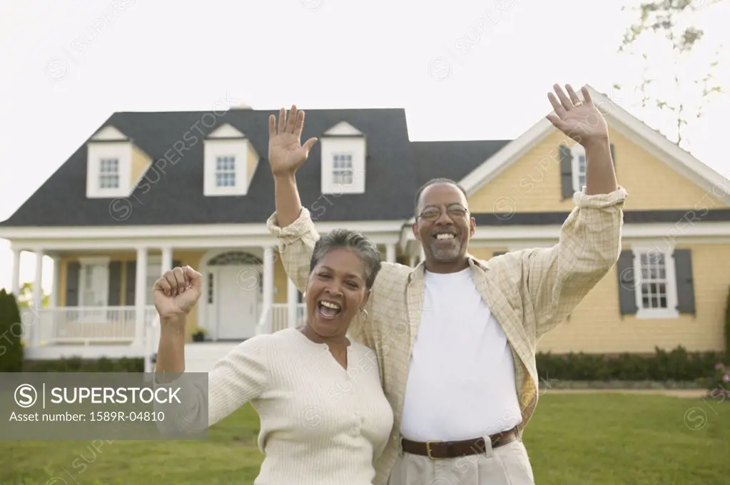 Portrait of a mature couple standing together with their arms raised in front of a house