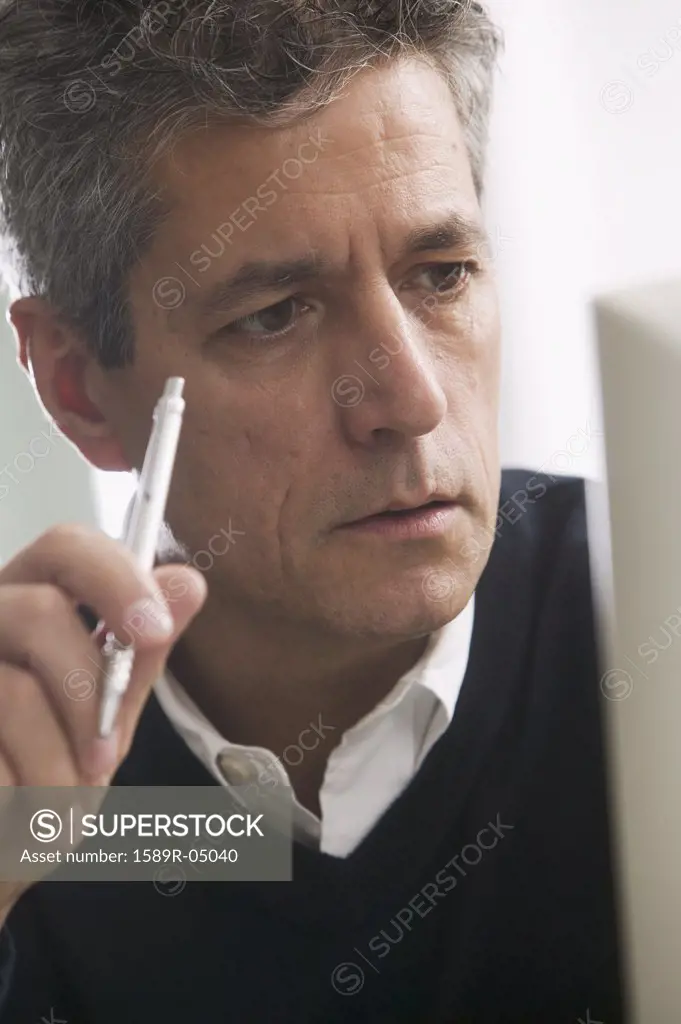 Man holding a pen looking at a computer screen