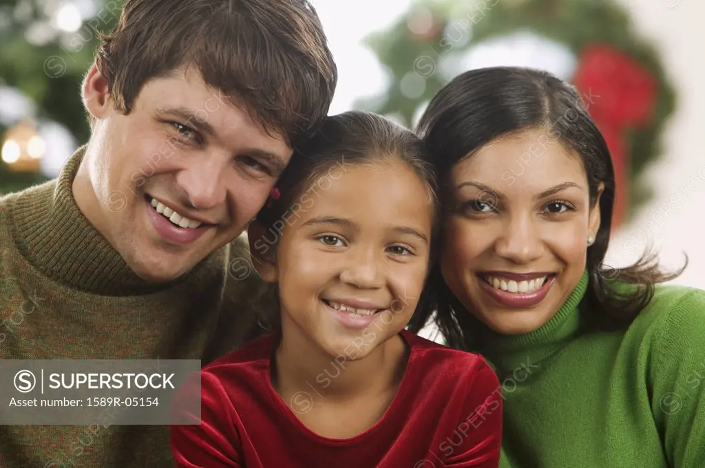 Young couple and their child looking at camera smiling with a Christmas tree in the background