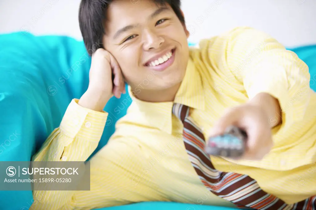 Businessman lying on a couch operating a remote control