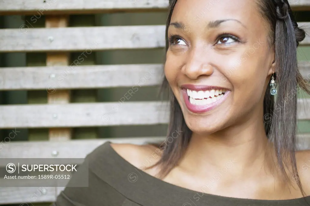 Young woman standing against a wooden structure smiling
