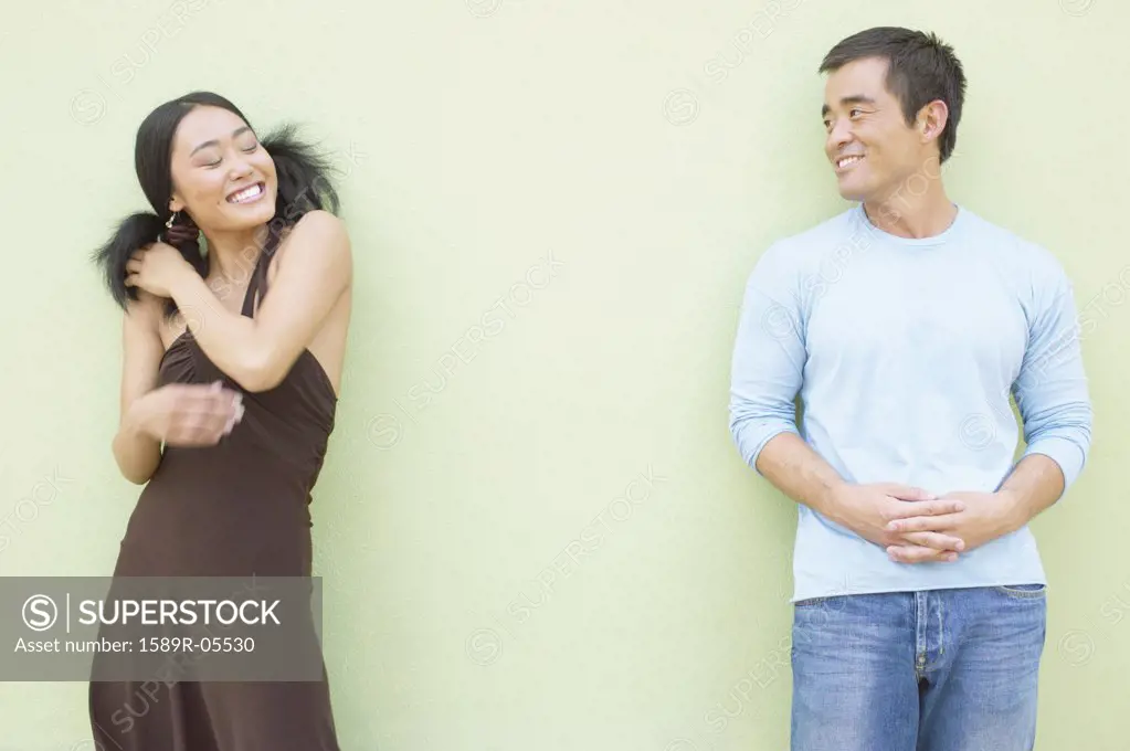 Young woman and a mid adult man standing against a wall smiling