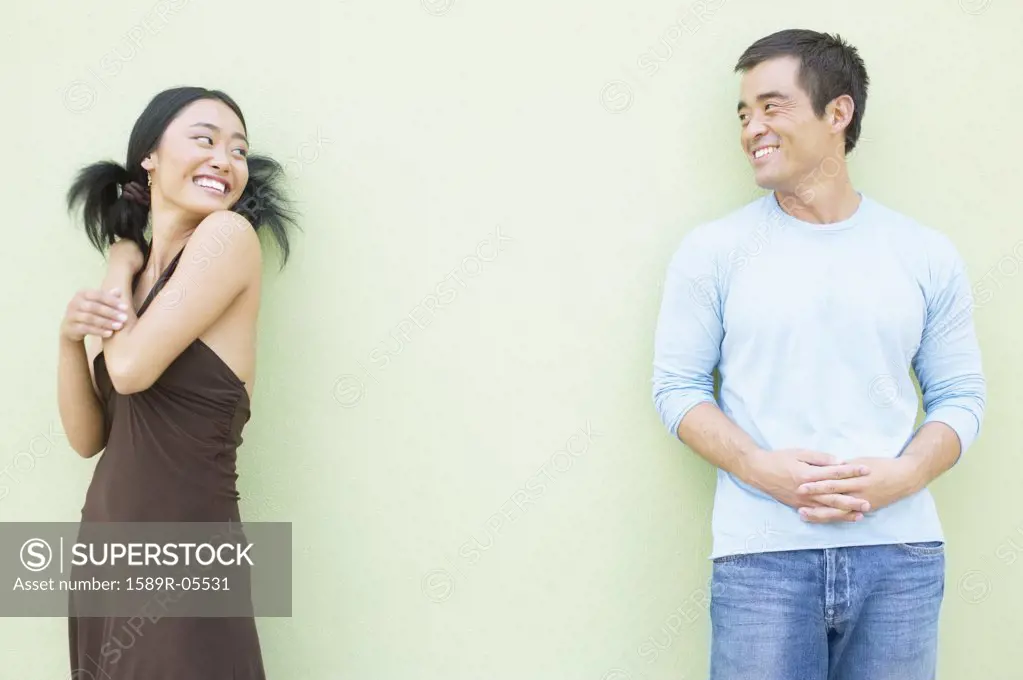 Young woman and a mid adult man standing against a wall smiling