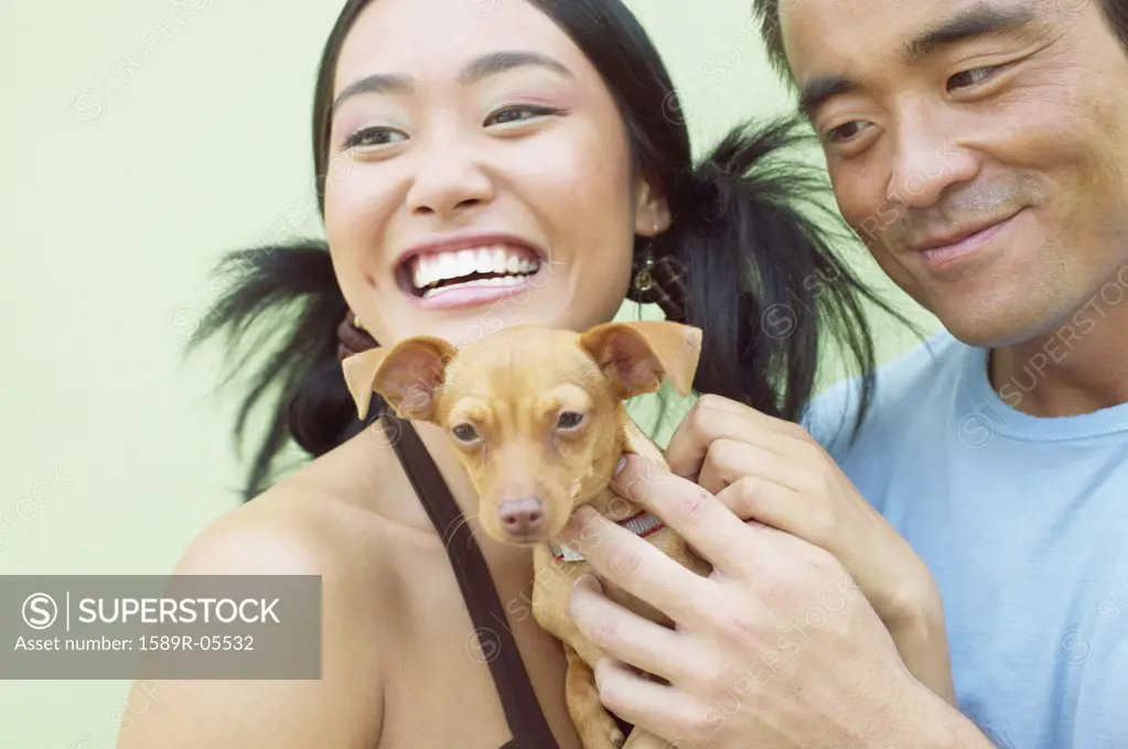 Young woman and a mid adult man standing together holding a puppy dog