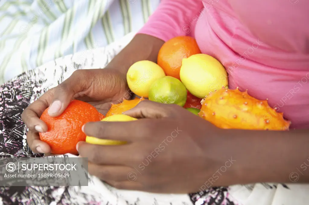 Mid section view of young woman holding fruit in her lap
