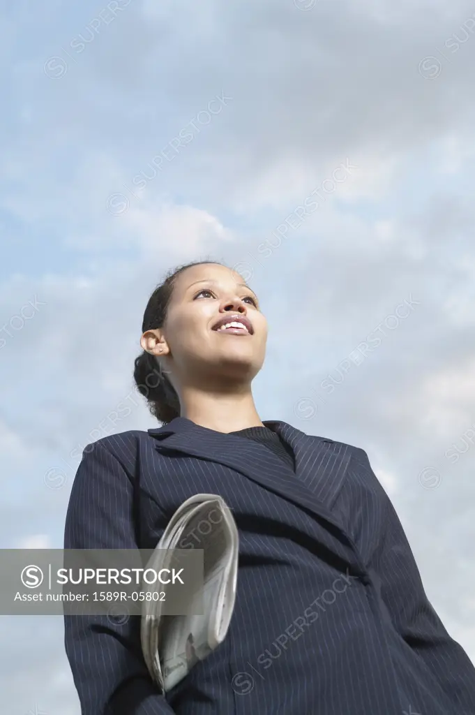 Low angle view of a young businesswoman smiling with a newspaper under her arm