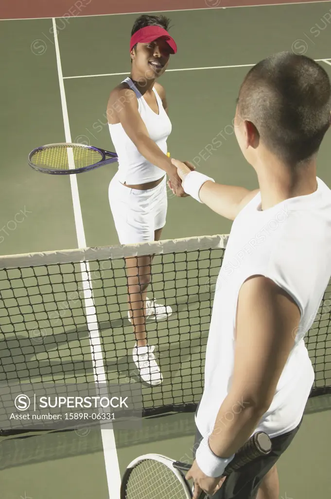 Young man and a young woman shaking hands over a tennis net