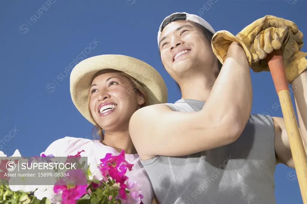 Young couple standing together in a garden holding potted plants smiling