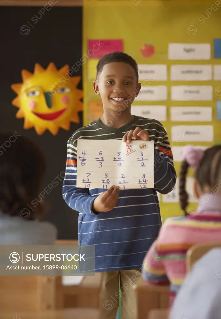 Boy standing in front of a class holding a sheet of paper