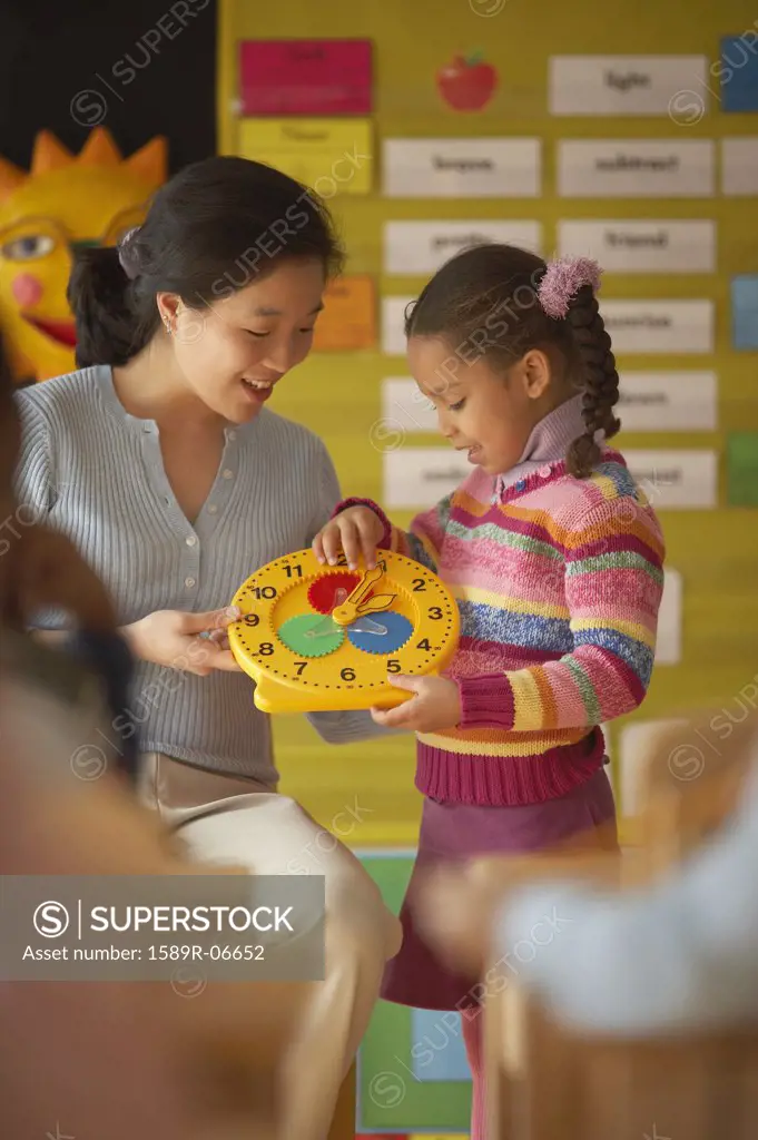 Female teacher and her student holding a toy clock