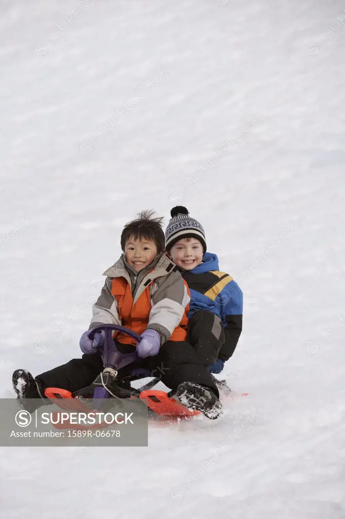 Portrait of two boys sliding down a hill on a toboggan