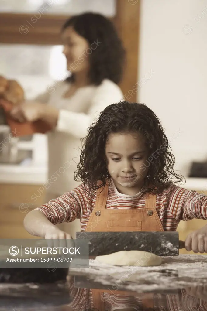 Girl rolling dough with her mother standing behind