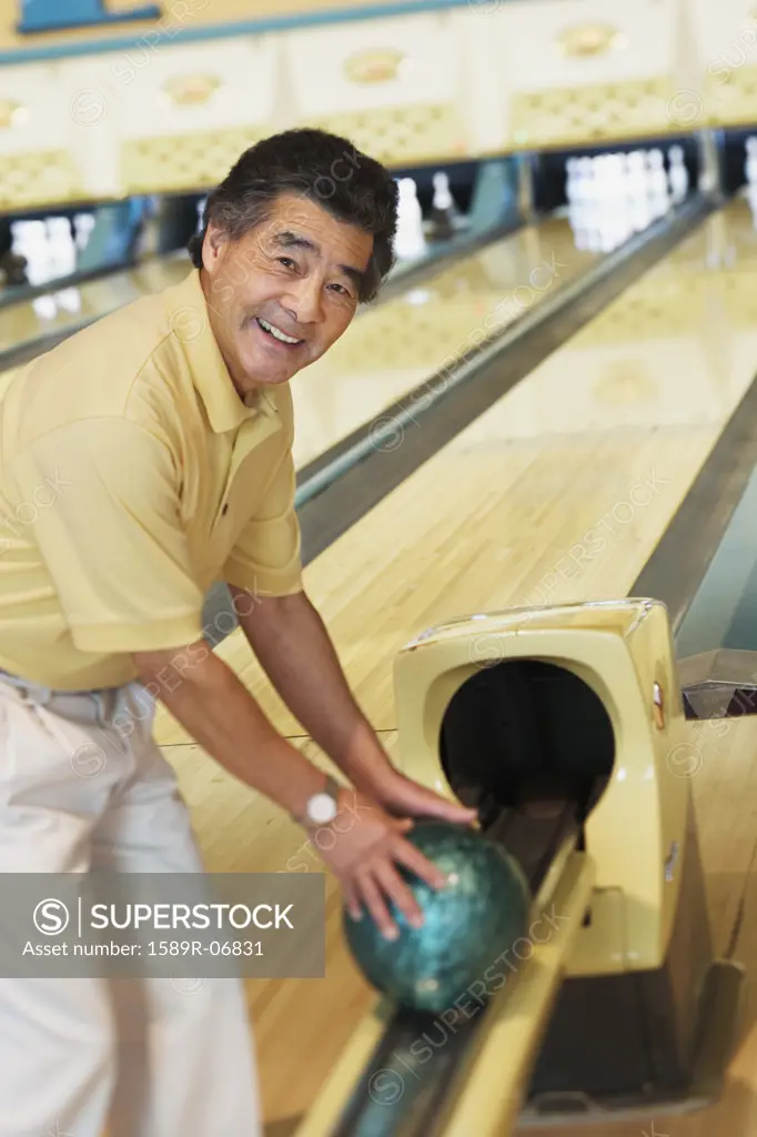 Portrait of a mature man taking a bowling ball from a channel in a bowling alley