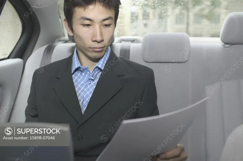 Mid adult businessman sitting in a car with a laptop in front of him