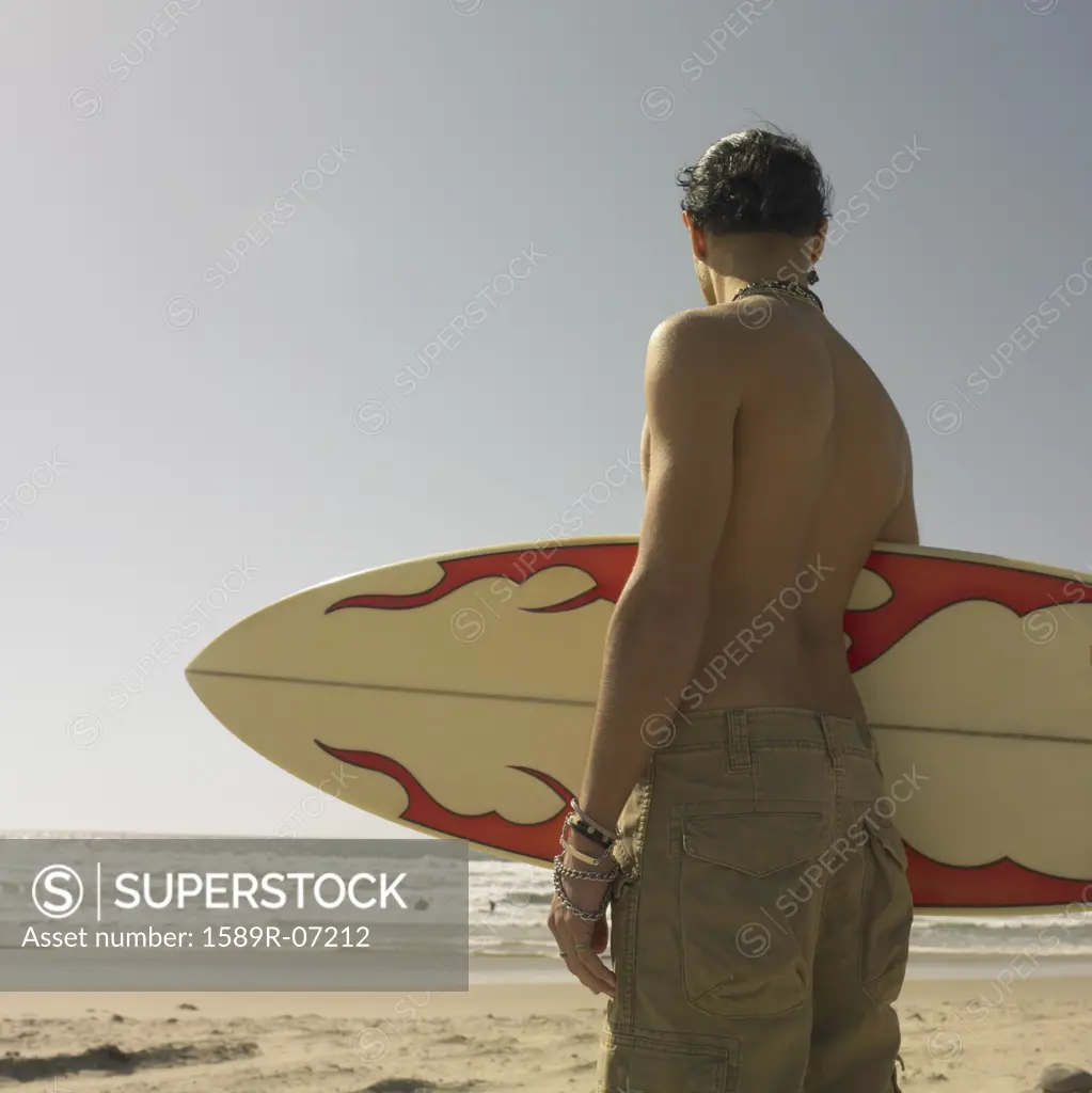 Rear view of a young man carrying a surfboard on the beach