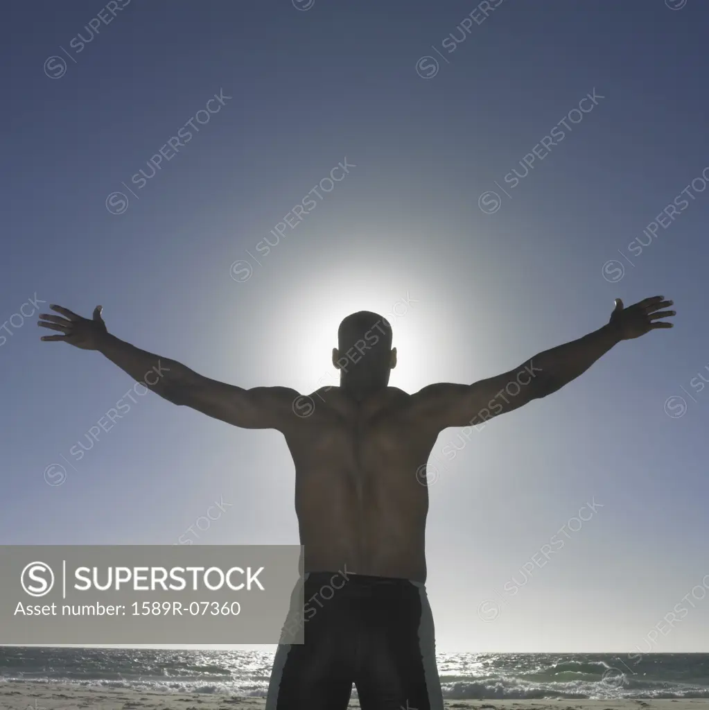 Rear view of a young man standing on the beach with his arm outstretched