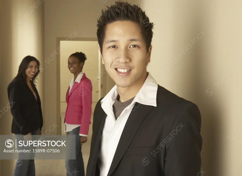 Portrait of a businessman smiling with two businesswomen standing behind him
