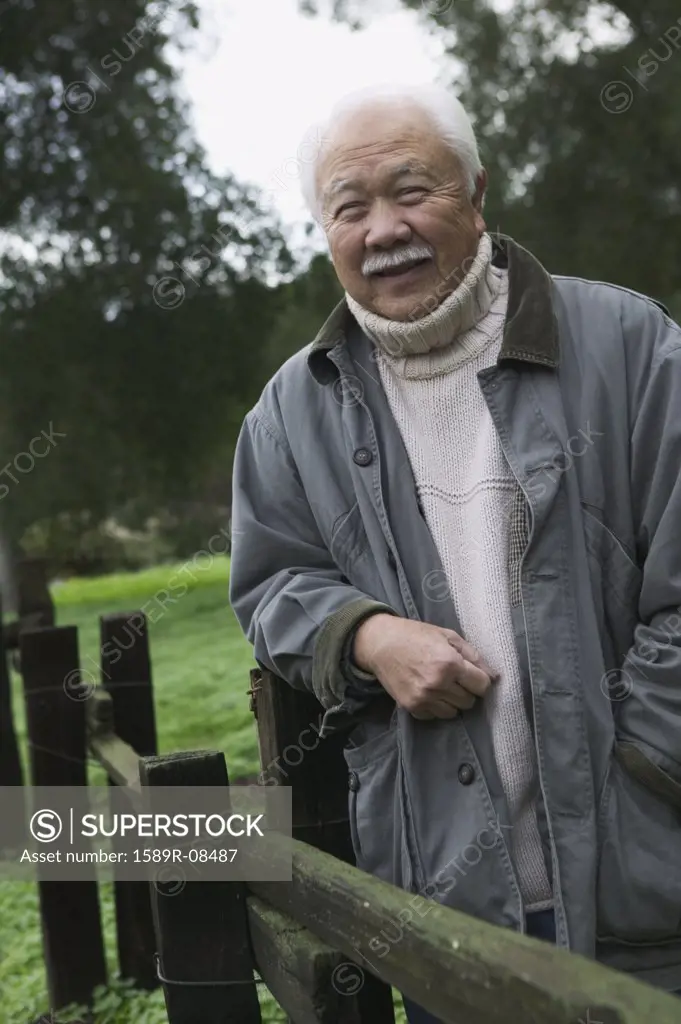 Portrait of a senior man leaning against a fence