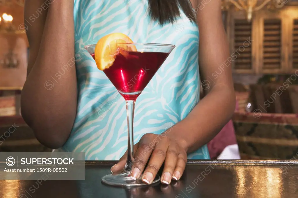Mid section view of a young woman standing at a bar counter with a martini glass