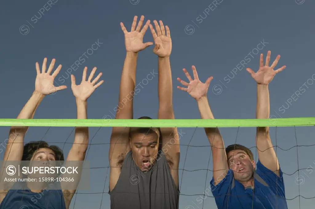 Young men jumping with their hands raised over a volley ball net