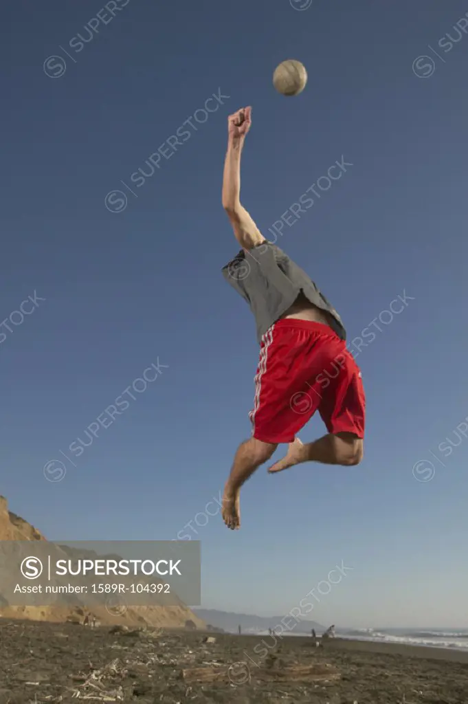 Low angle view of a young man jumping up in the air reaching for a volleyball