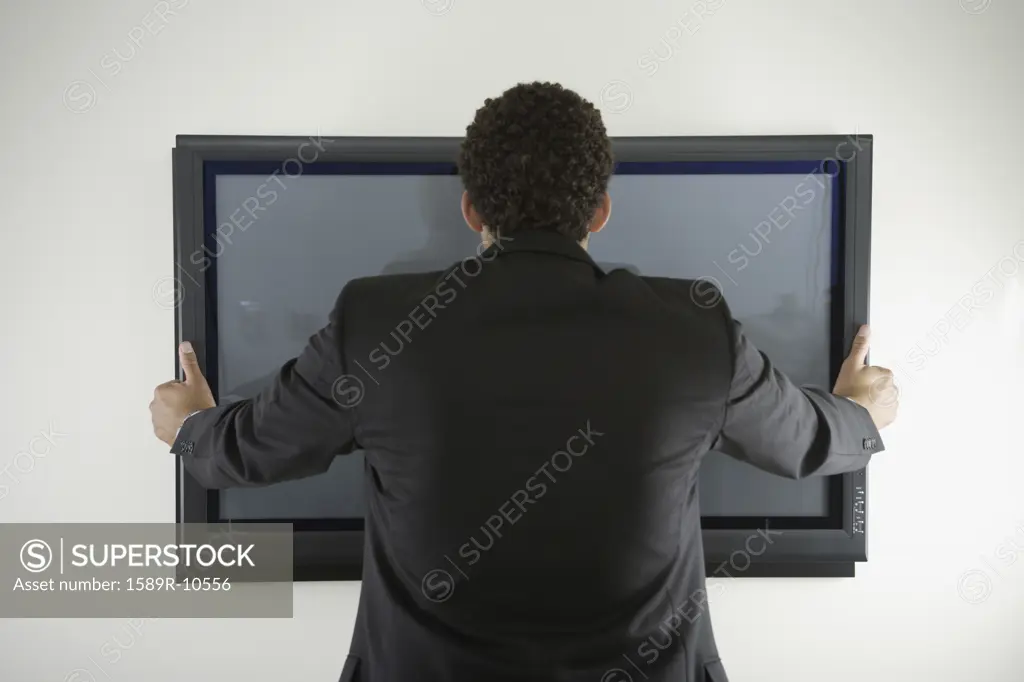 Rear view of man hanging flat screen on wall