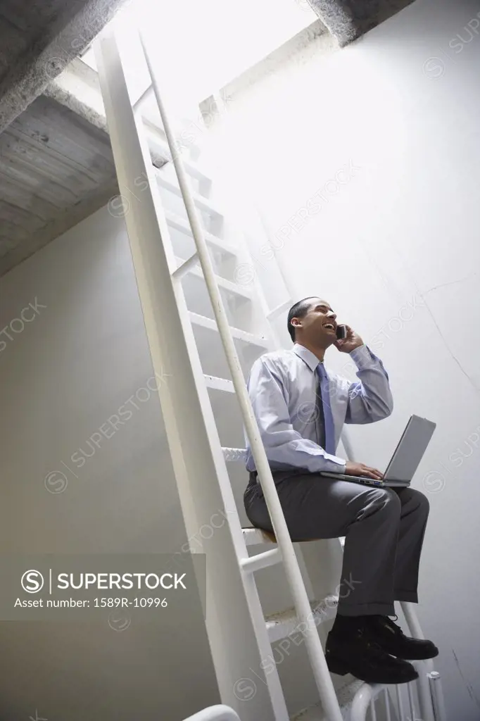 Man on ladder with laptop and mobile phone