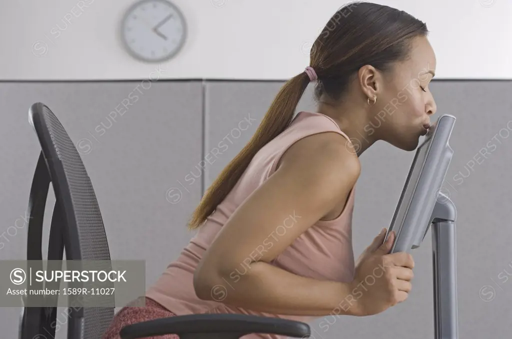 Woman in office kissing computer monitory