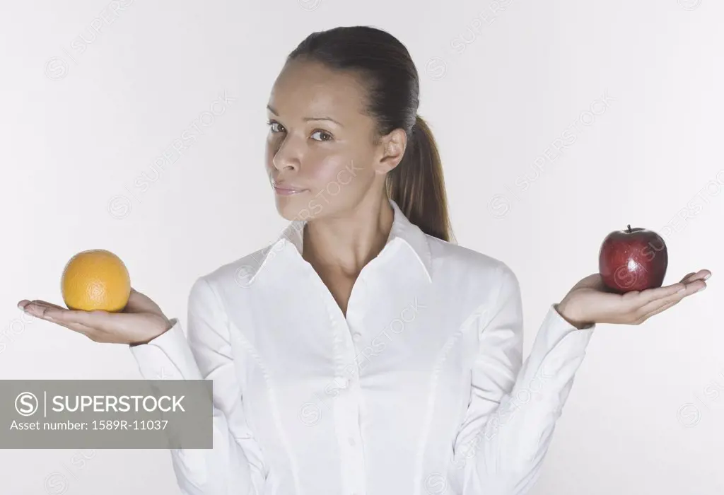 Portrait of woman balancing orange and apple in hands