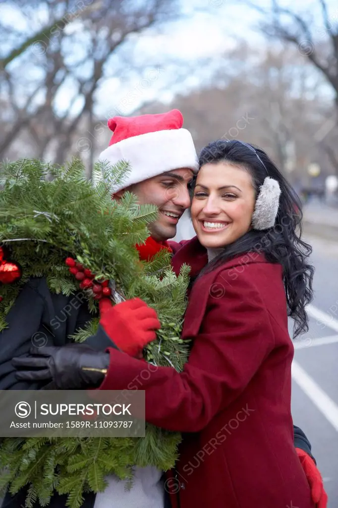 Couple carrying Christmas wreath on city street
