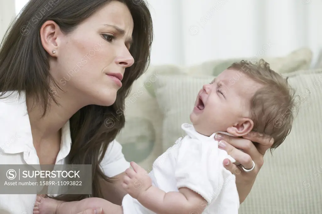 Mother comforting crying baby on sofa