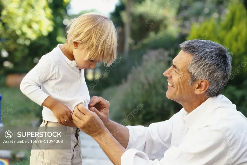 Caucasian father buttoning son's shirt outdoors
