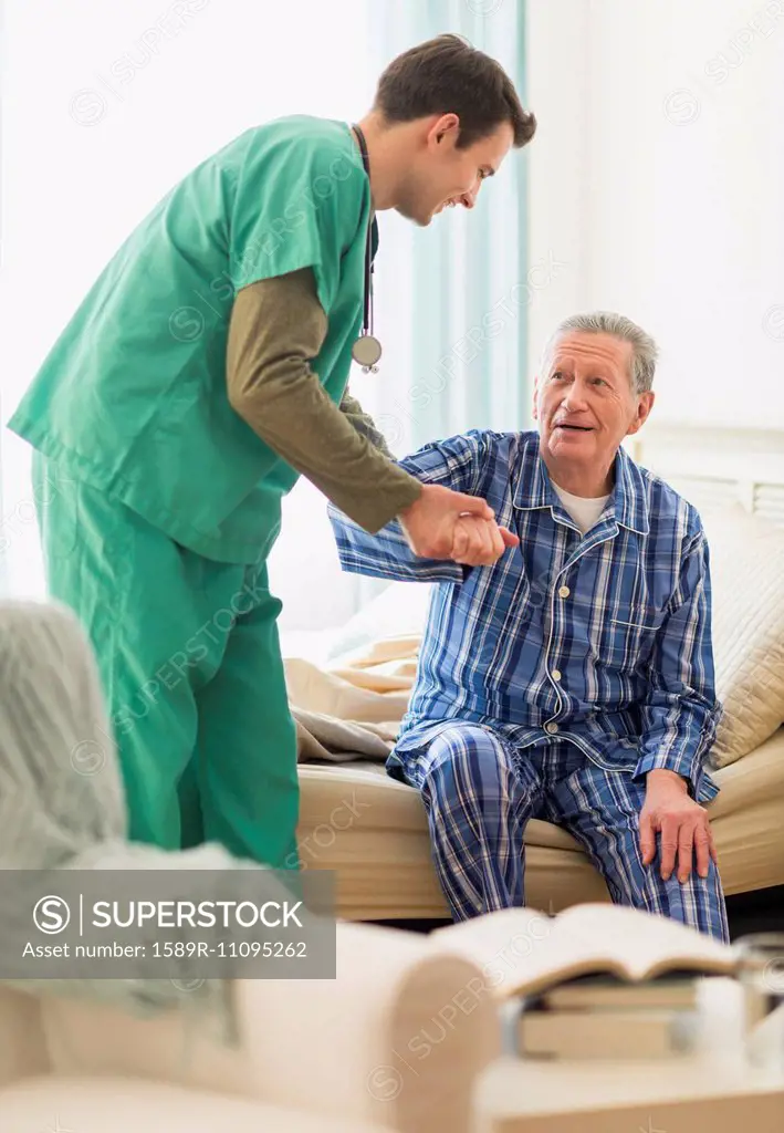 Caucasian nurse helping patient out of bed in home