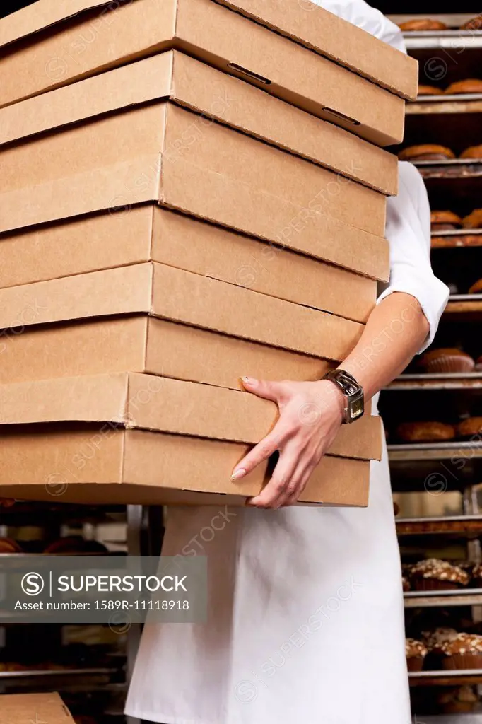 Hispanic baker carrying stack of boxes in bakery