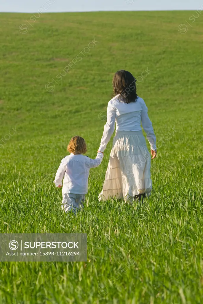 Mother and son holding hands in field rear view