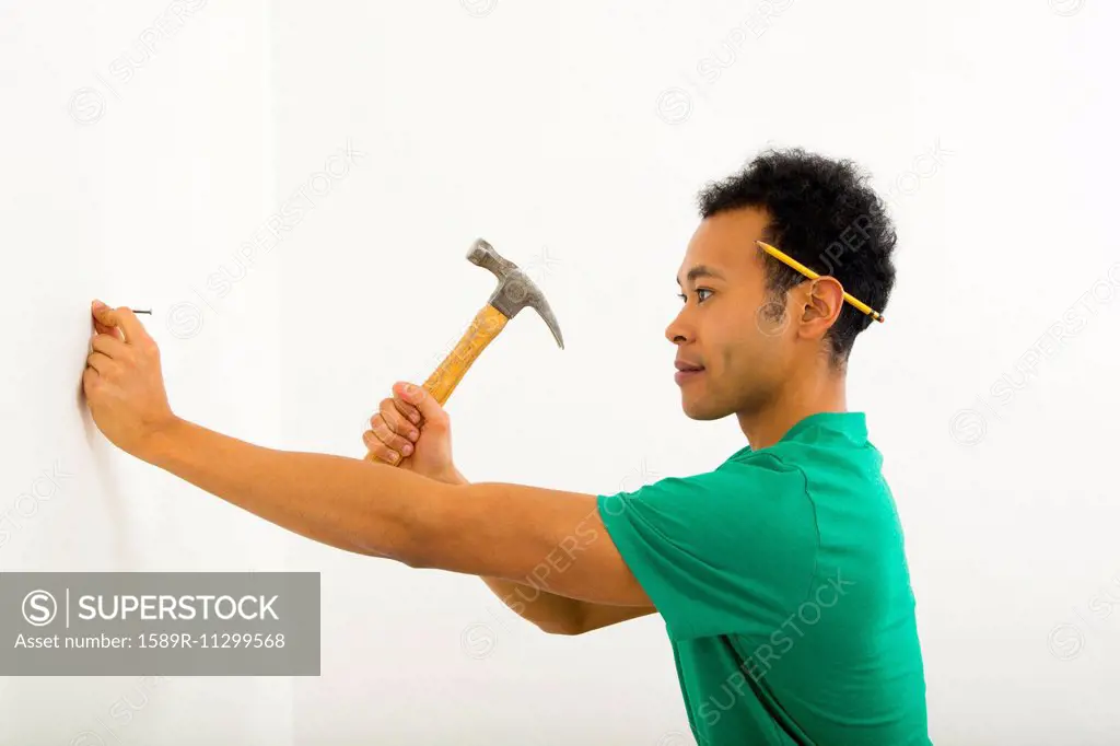 Mixed race man hammering nail into wall