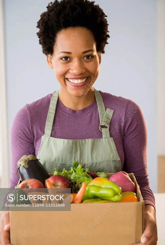 Portrait of Black woman holding box of vegetables
