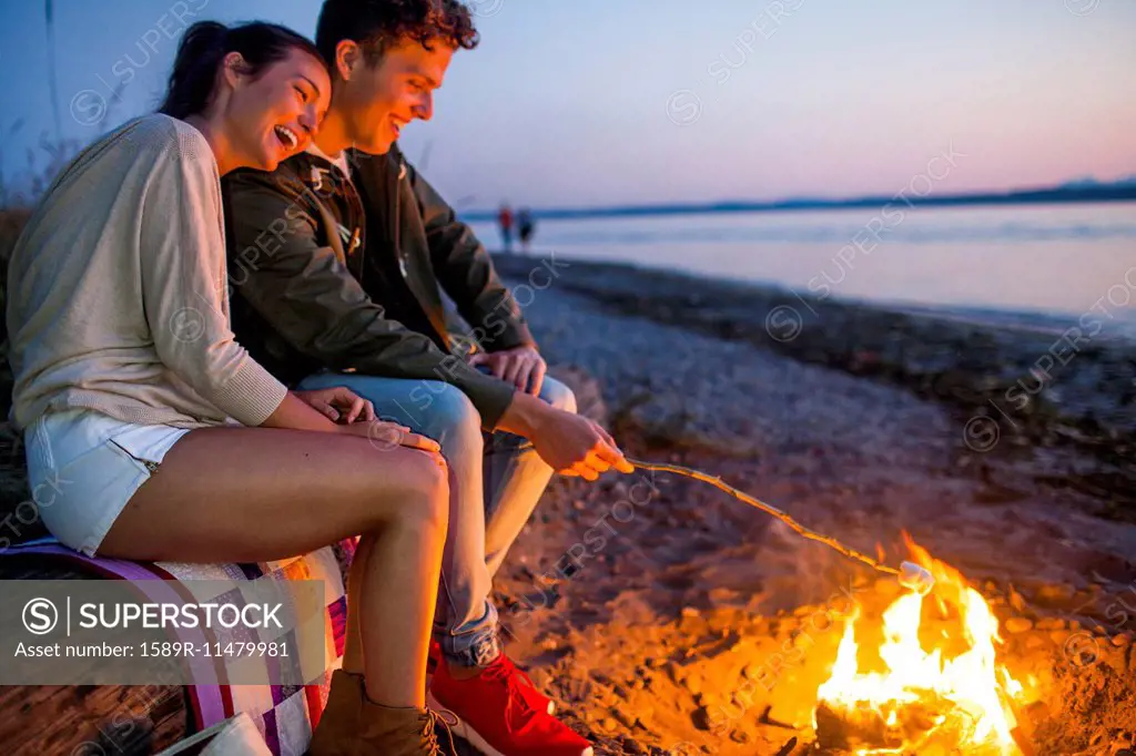 Caucasian couple roasting marshmallows on fire at beach
