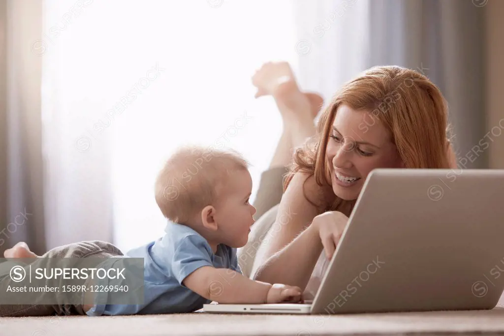 Caucasian mother and son using laptop on floor